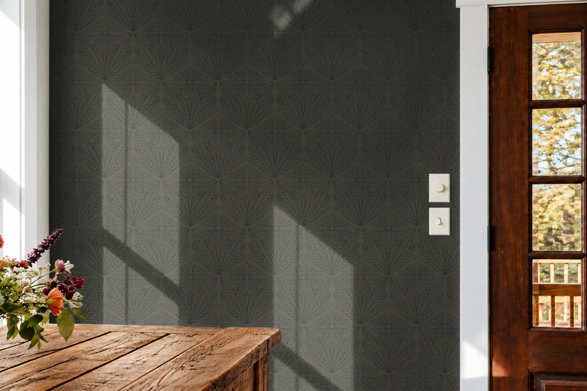 muted olive green wallpaper featuring an intricate Art Deco-inspired geometric floral pattern in a sunlit entryway with a rustic wood table and dark wood glass-paneled door.