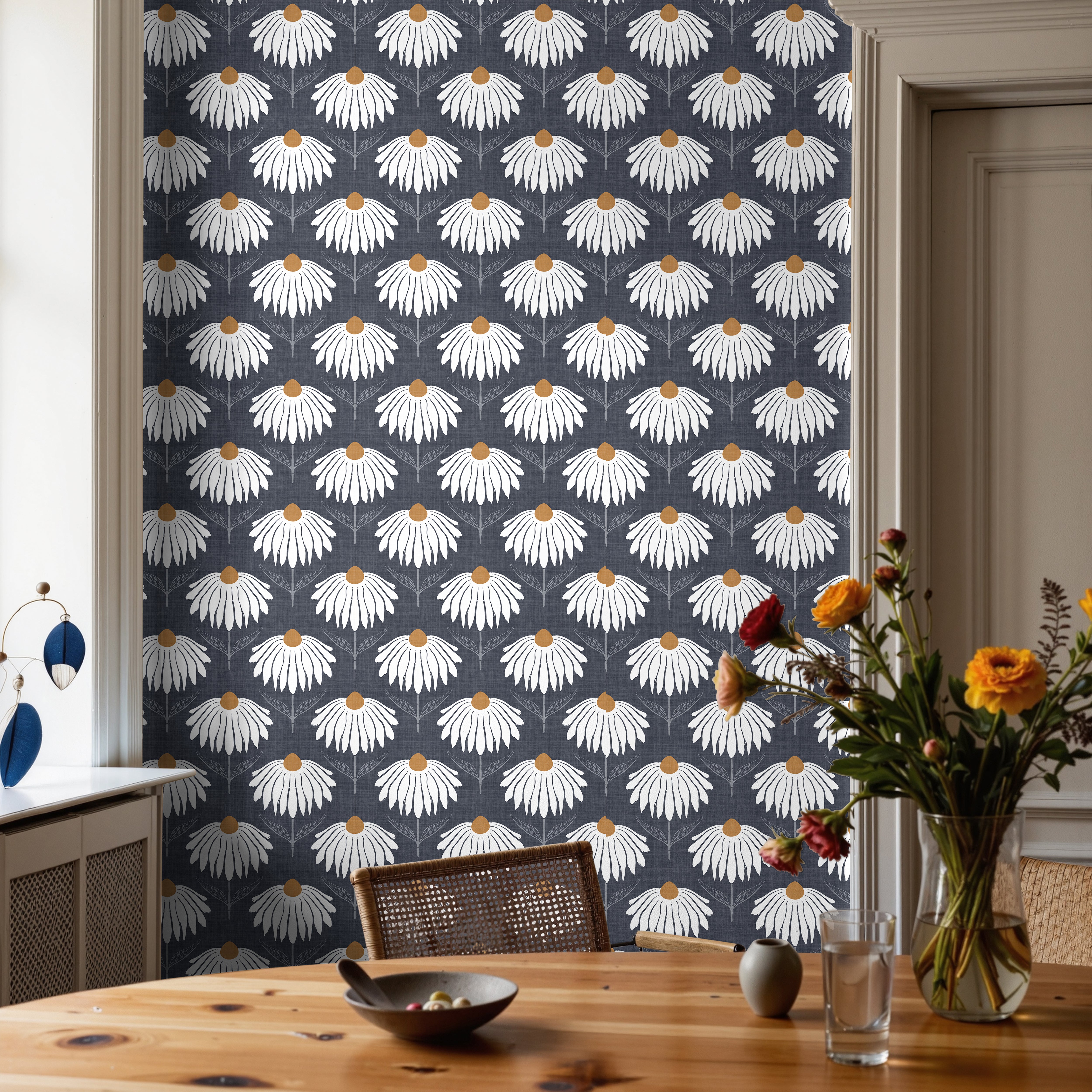Chantelune Noir 2249 navy blue floral wallpaper featuring repeating white coneflowers with warm golden centers, styled in a dining room with a natural wood table, woven chairs, and a colorful floral arrangement.