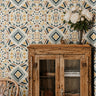 Geometric Boho 2377 wallpaper featuring a colorful bohemian geometric pattern in mustard yellow, muted teal, terracotta, and cream, styled in a dining room with a rustic wooden cabinet and white flowers.