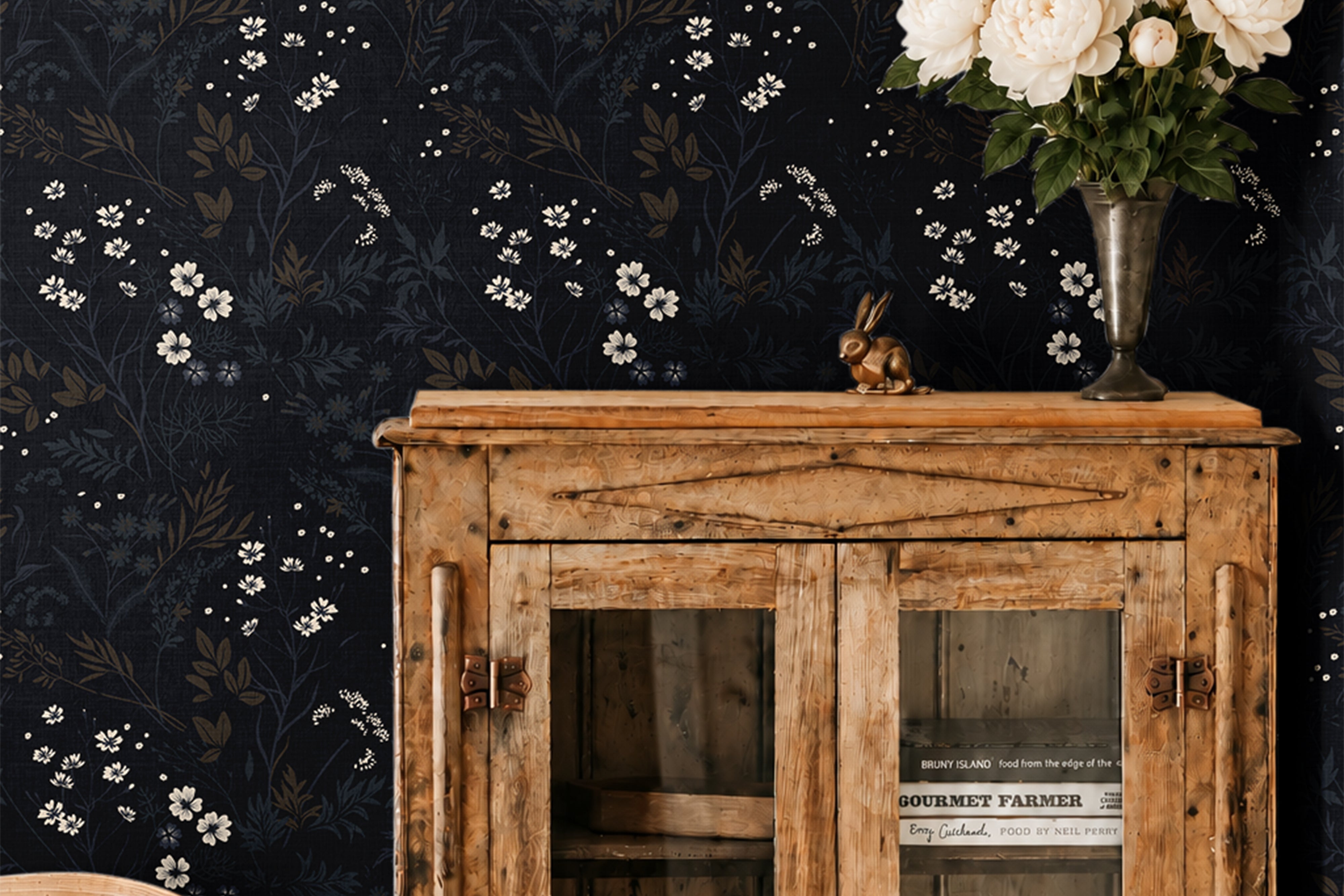ink and elderflower 3552 moody floral wallpaper behind a rustic wood cabinet with white flowers in a vase and a wood chair
