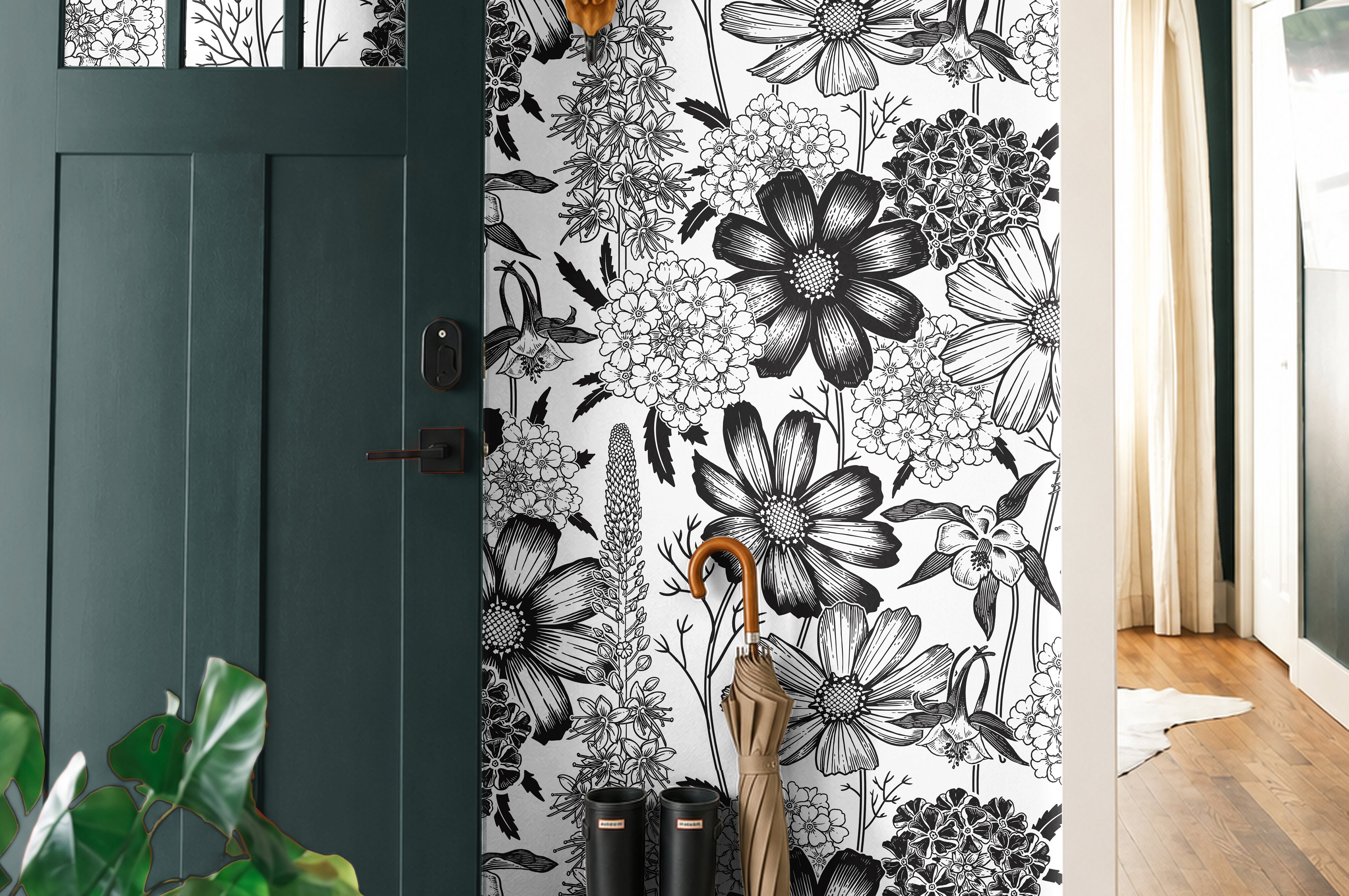 Monochrome Meadow 764 black and white botanical wallpaper featuring oversized vintage wildflowers and detailed floral illustrations, styled in a modern entryway with a dark green door, natural wood flooring, black rain boots, and an umbrella.