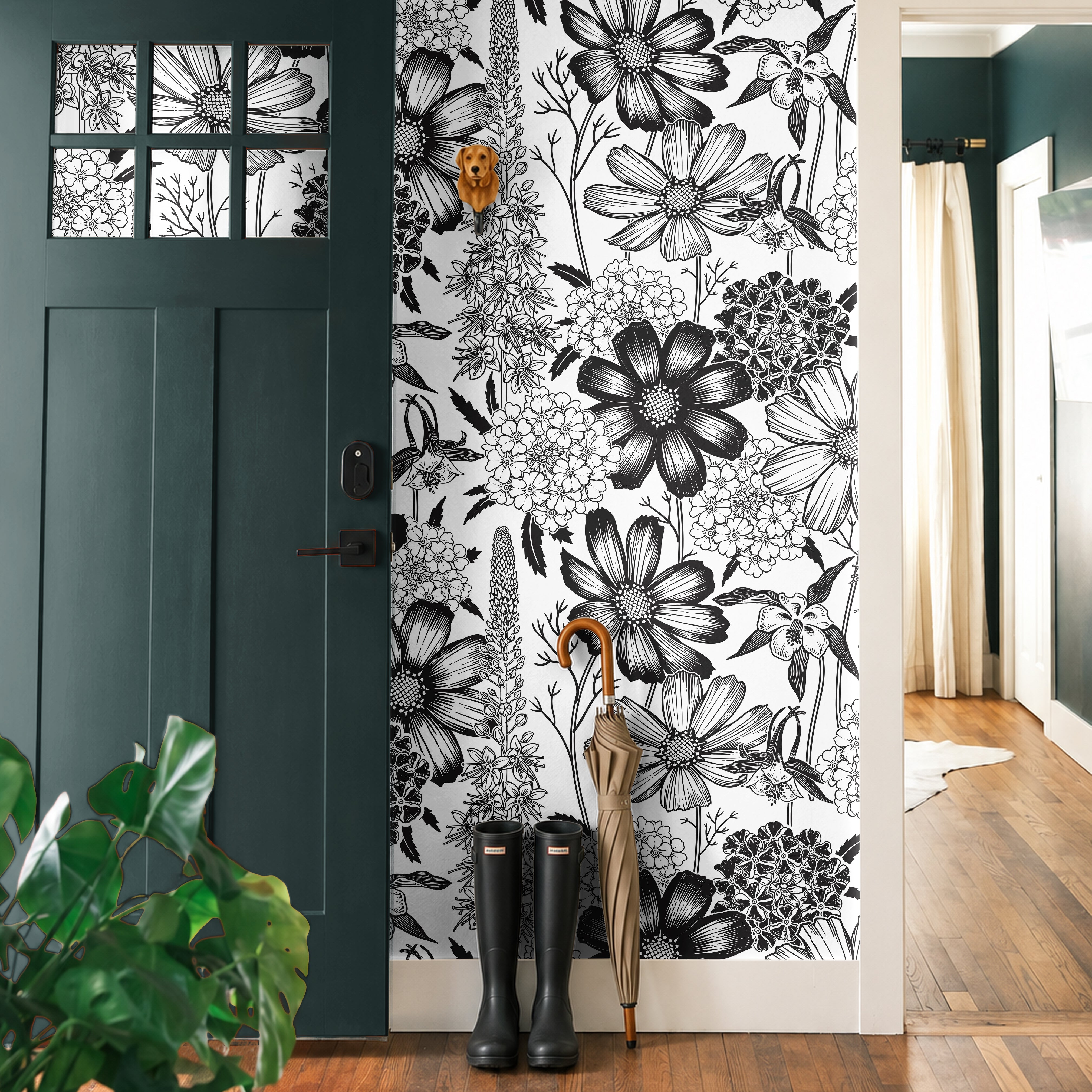 Monochrome Meadow 764 black and white botanical wallpaper featuring oversized vintage wildflowers and detailed floral illustrations, styled in a modern entryway with a dark green door, natural wood flooring, black rain boots, and an umbrella.