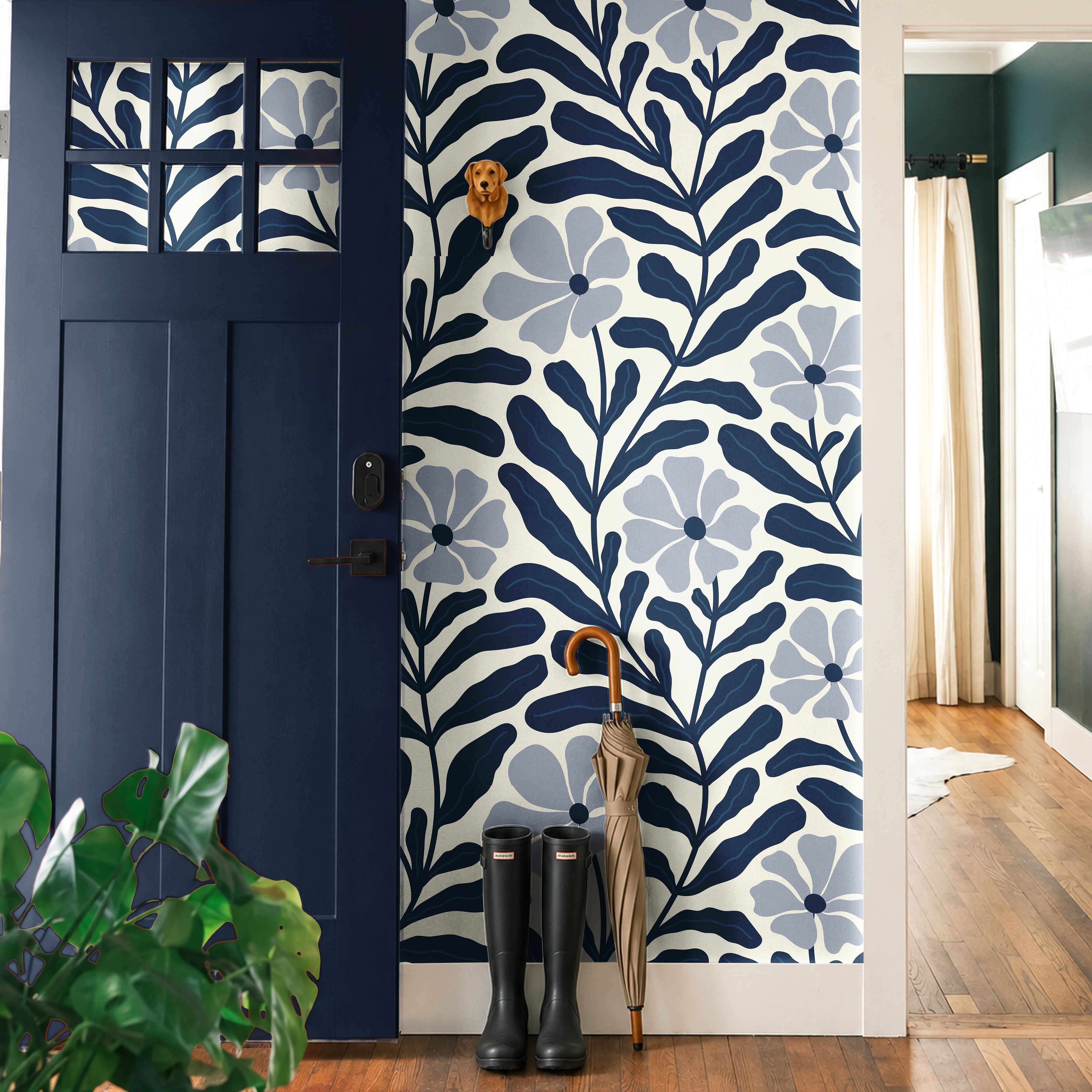 Navy Nature Floral 540 wallpaper featuring oversized dusty blue flowers and dark navy botanical leaves on a cream background, styled in a modern entryway with a navy blue door, natural wood floors, and black rain boots.
