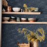 navy abstract line wallpaper behind open wood kitchen shelves with blue dishes black faucet and white
counter